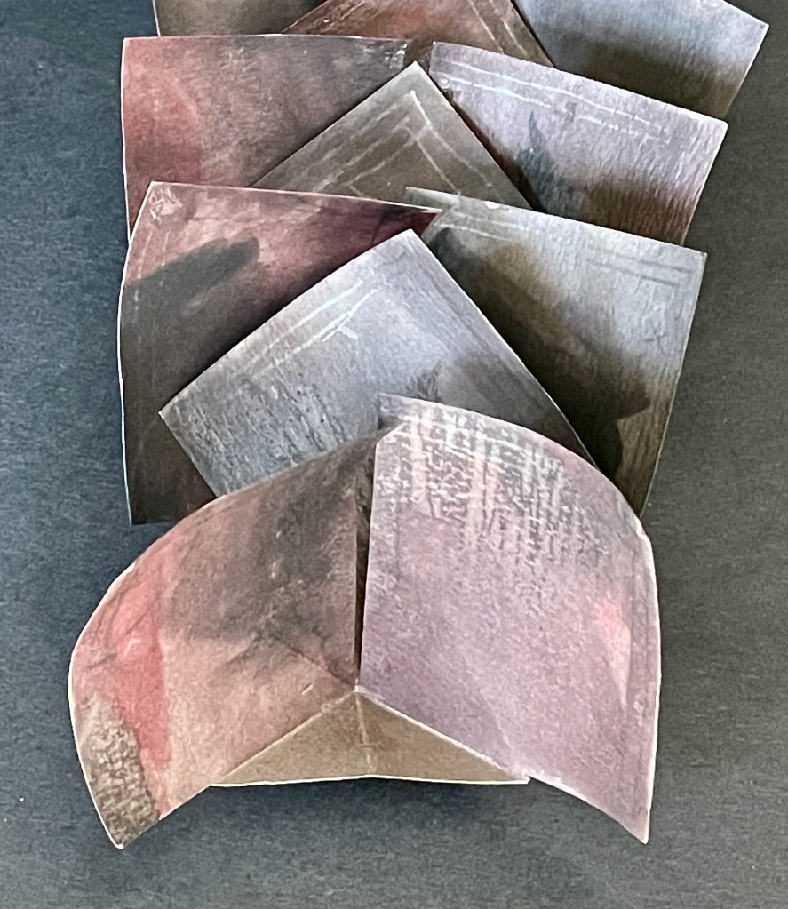 An arrangement of layered, textured paper shapes in various shades of brown and gray, placed on a dark background.