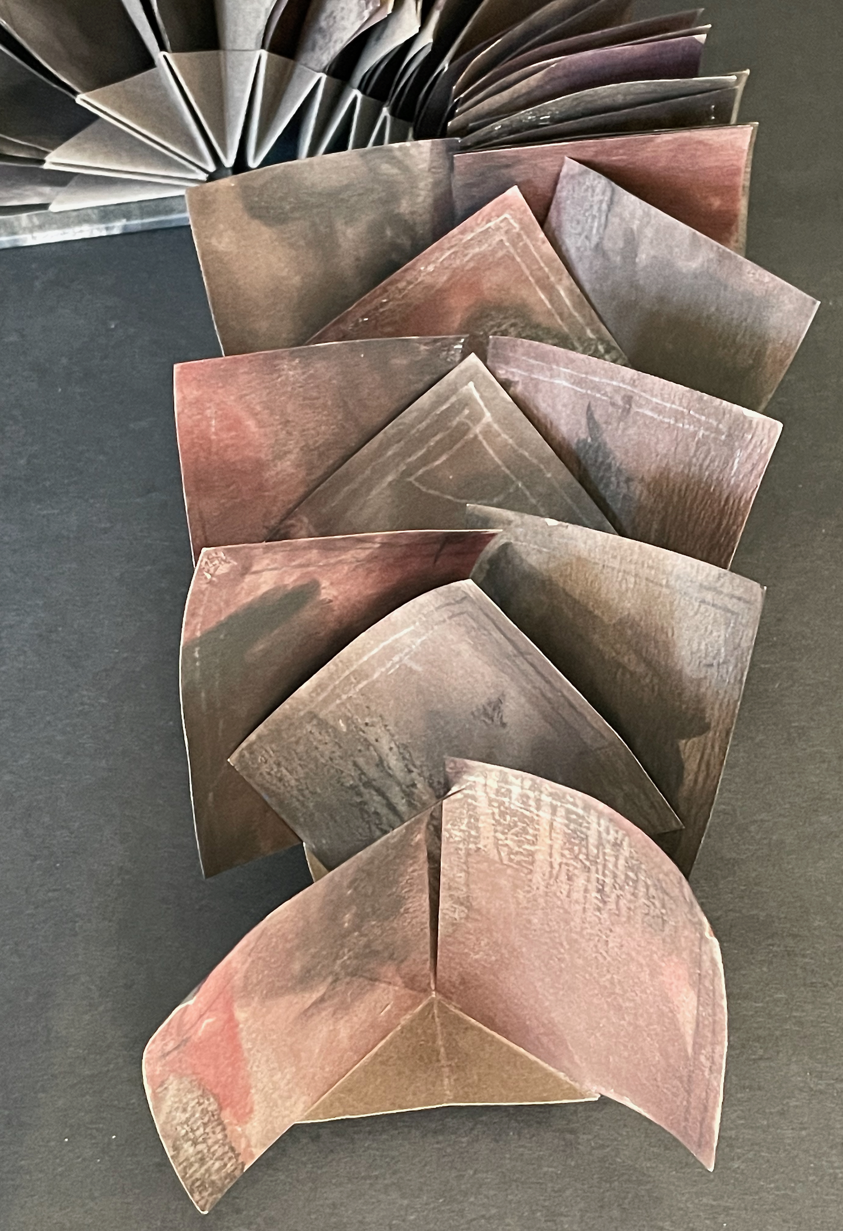 A close-up of several folded paper pieces arranged in a spiral, showcasing a mix of brown and reddish tones on a black background.