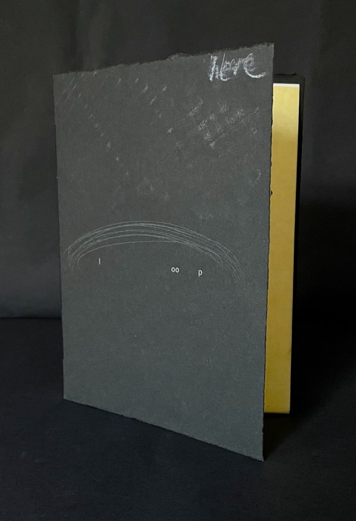 A closed book with a black cover featuring minimal text and a gold spine, resting on a black surface.