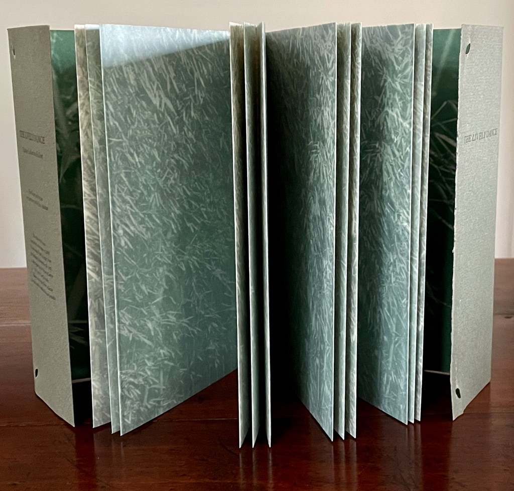 Close-up view of a book with textured green pages, partially open, sitting on a wooden surface.