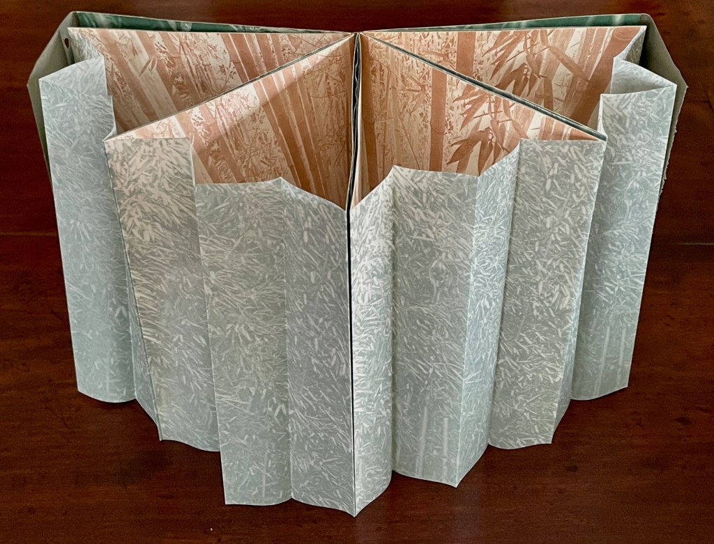 An open accordion-style book with textured green and beige pages, showcasing a bamboo forest illustration.