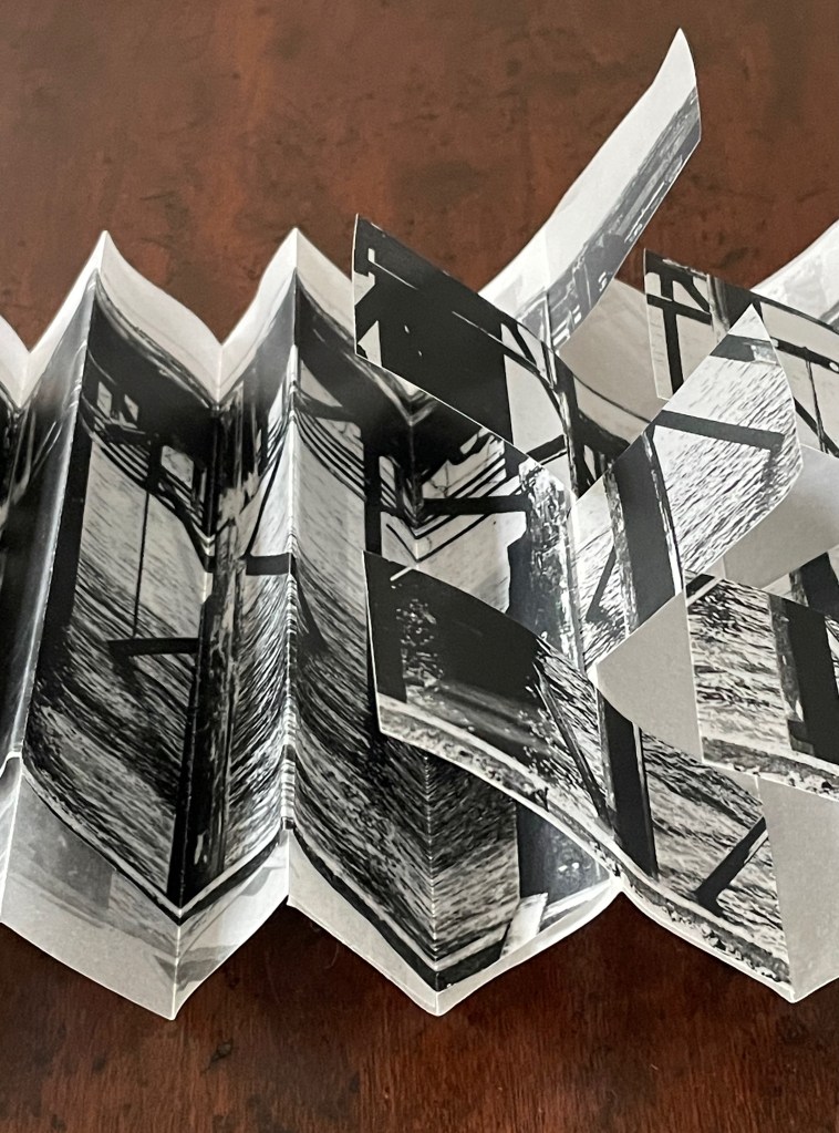 A folded book or art piece featuring black and white photographs, displayed on a wooden surface.