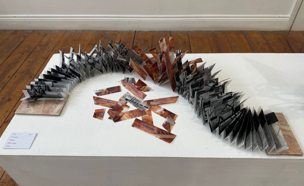 An artistic display featuring a sculptural book made of layered, folded paper in various colors, arranged in a wave-like formation with scattered pieces nearby.