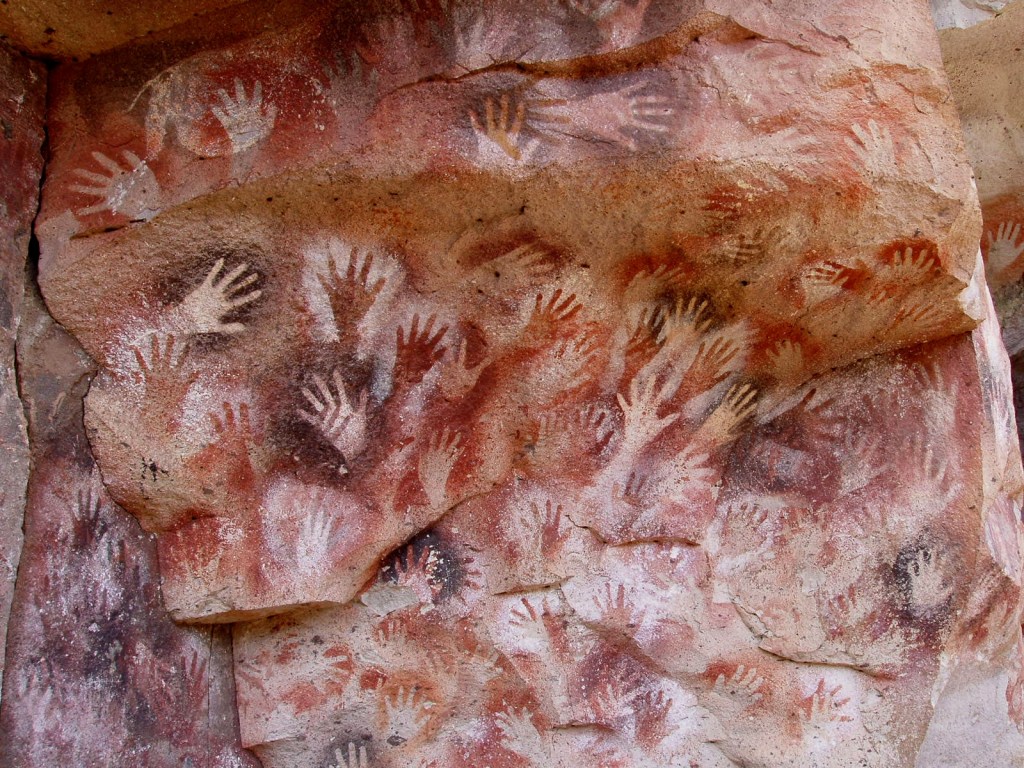 Cave wall covered with ancient handprints in various colors, showcasing prehistoric art.