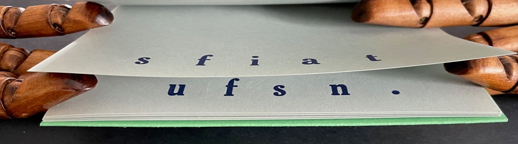A close-up of a wooden hand model holding pages with text printed on them, featuring the letters 's f i a t' on one page and 'u f s n .' on another.