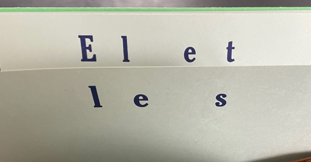 Close-up of two pages showing the letters E, l, e, t, l, e, s in blue on white paper.