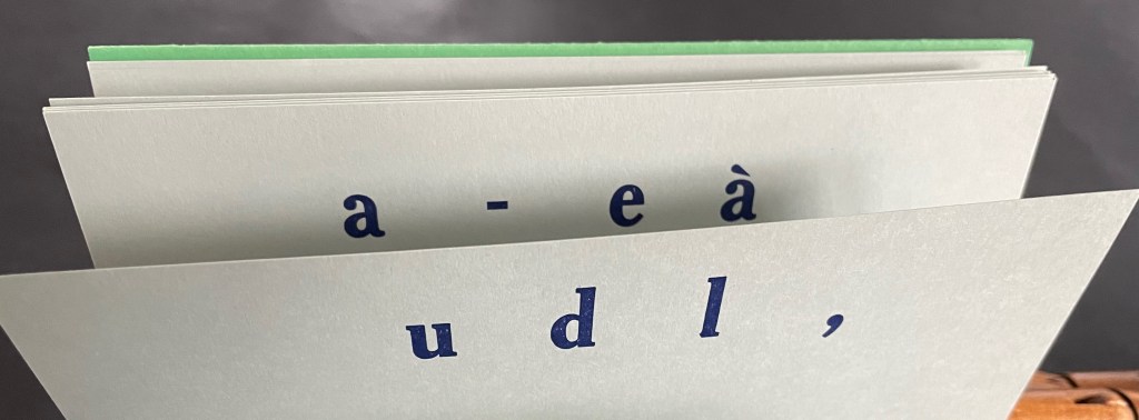 A close-up image of a stacked book or notebook featuring partially visible pages with printed text in blue, including letters and symbols.