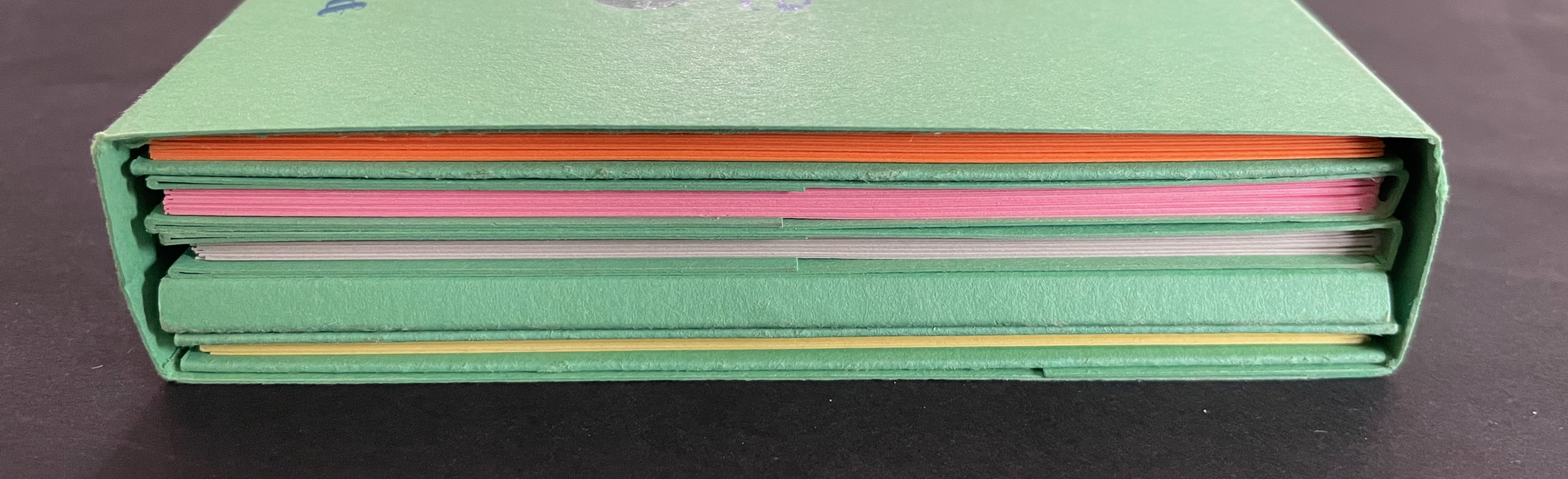 A stack of colorful paper sheets in assorted shades, neatly arranged within a green folder.
