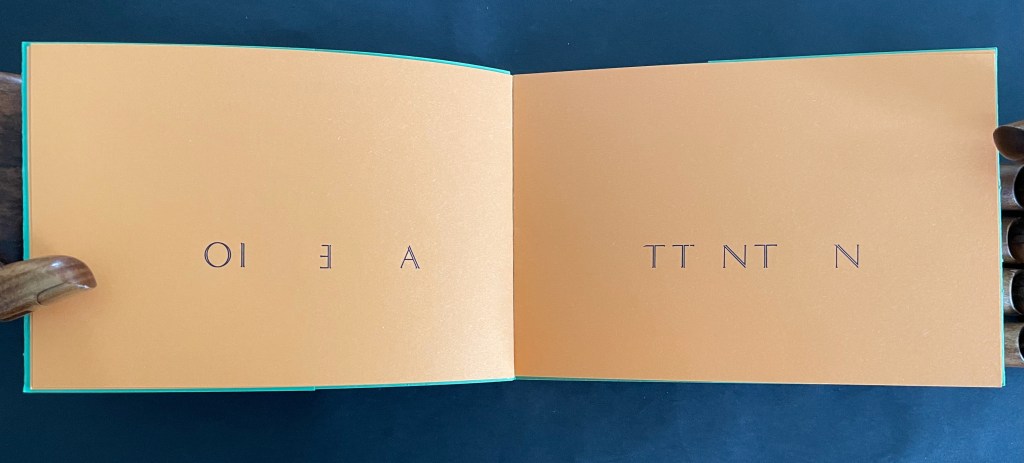 An open book with orange pages displaying text arranged in an unusual orientation, set against a dark background.