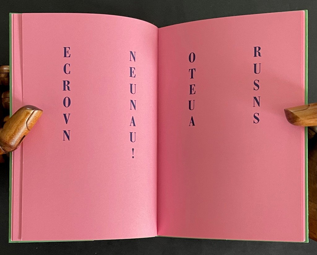 An open book with pink pages featuring vertically aligned text: 'ECROVN', 'NEUNAU!', 'OTEUA', and 'RUSNS'.