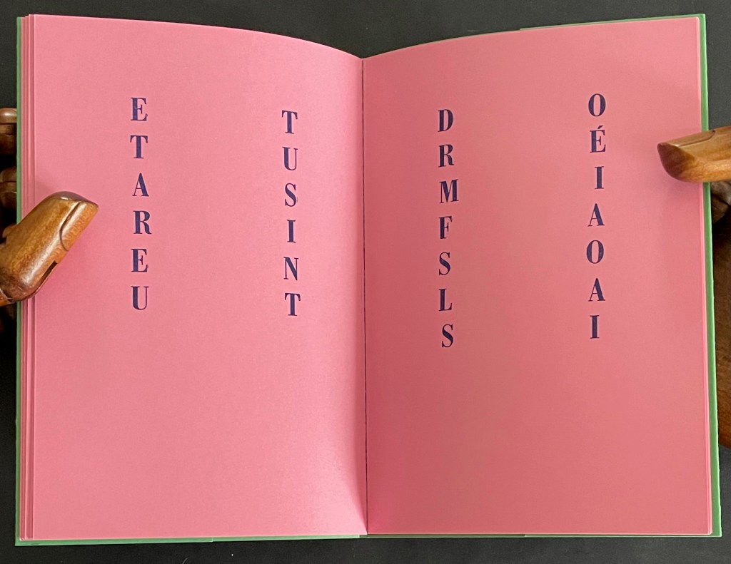 An open book with pink pages displaying vertically arranged text in blue letters.