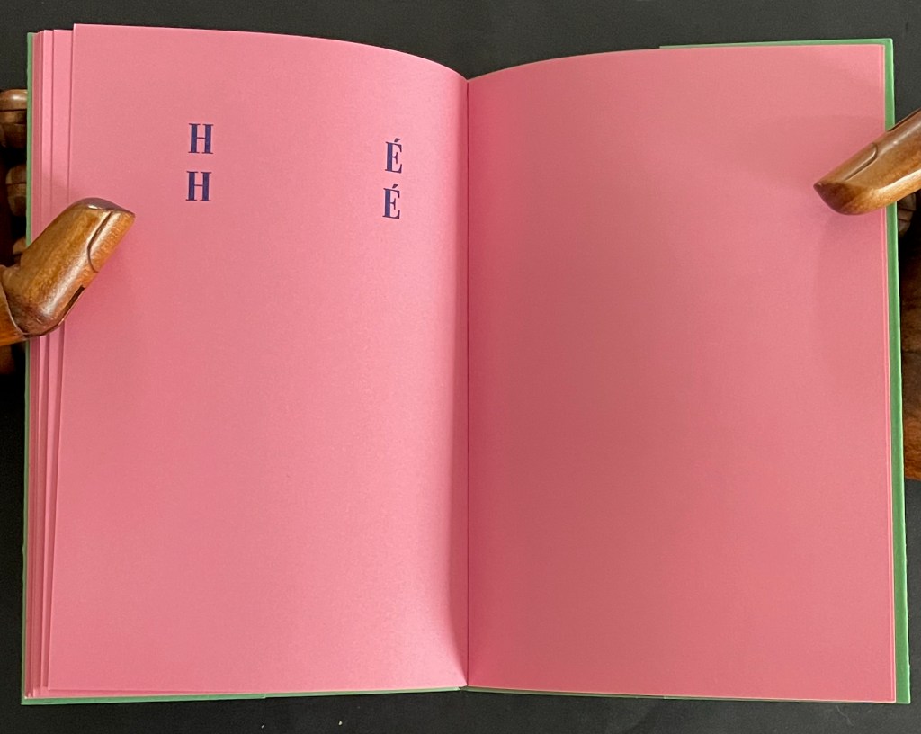 An open book with pink pages displaying the letters 'H' and 'É' on the left page.