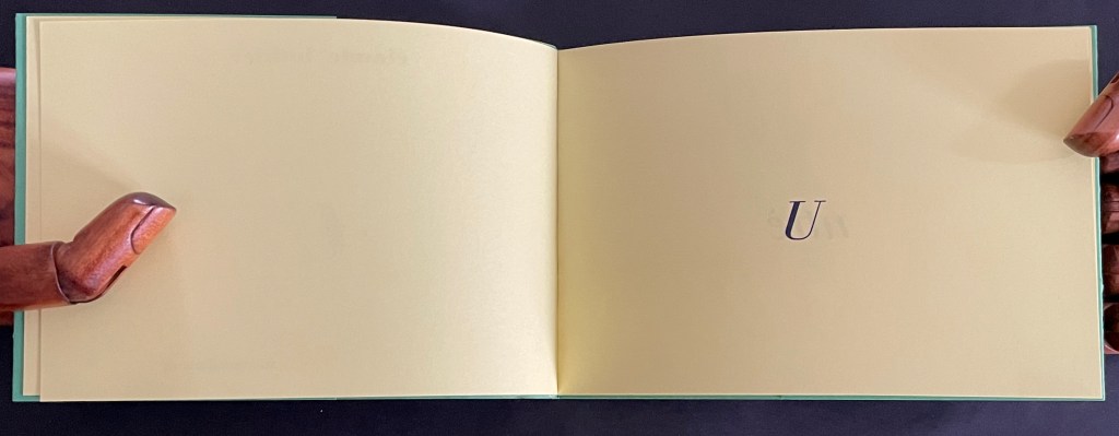 Open book with yellow pages featuring a single letter 'U' printed in the center.