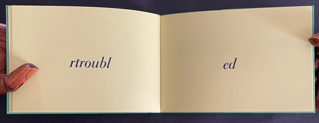An open book displaying the words 'rtroub' on the left page and 'ed' on the right page, with hands holding the pages.