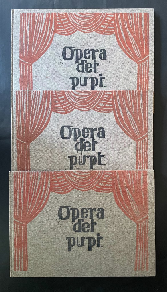 Three stacked books titled 'Opera dei Pupi', featuring a design of curtains in red on a textured beige background.