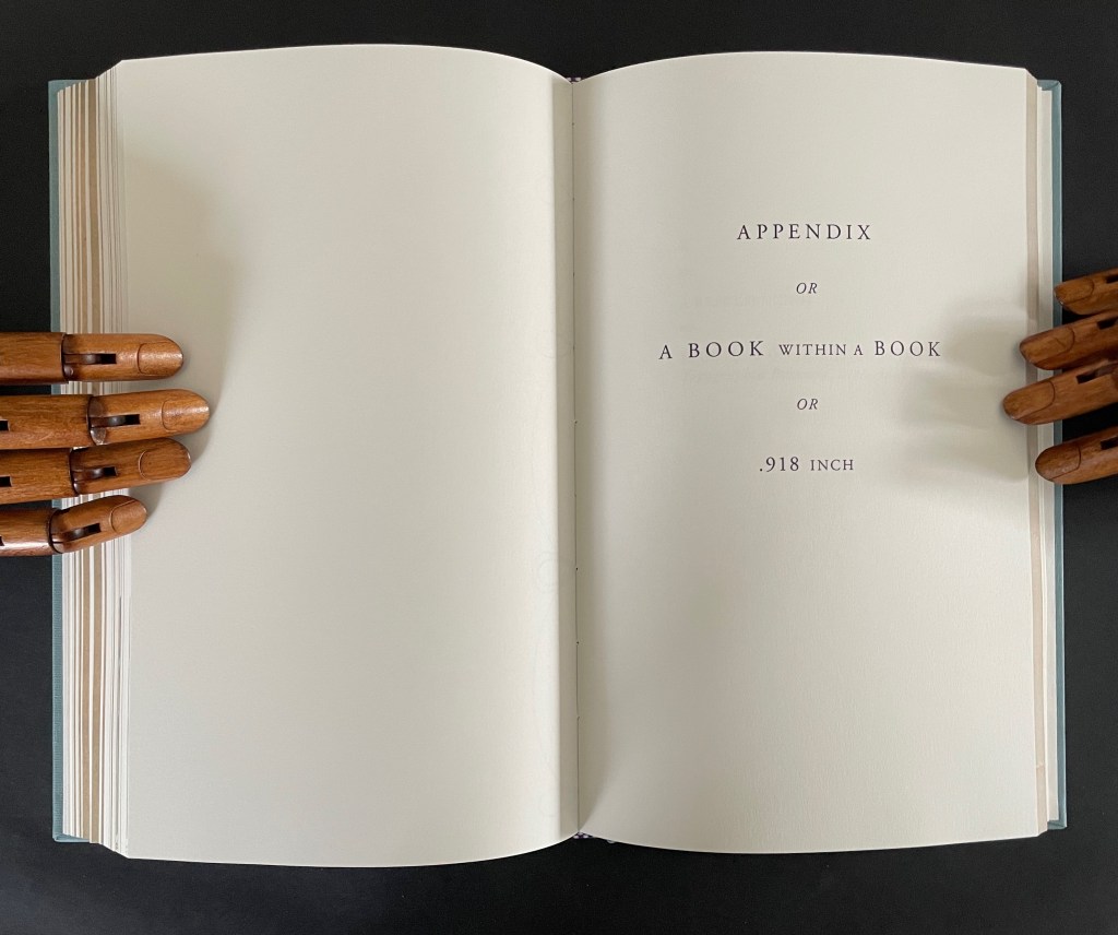 An open book page with the title 'APPENDIX OR A BOOK WITHIN A BOOK OR .918 INCH' printed in an elegant font, accompanied by wooden articulated hands holding the book.