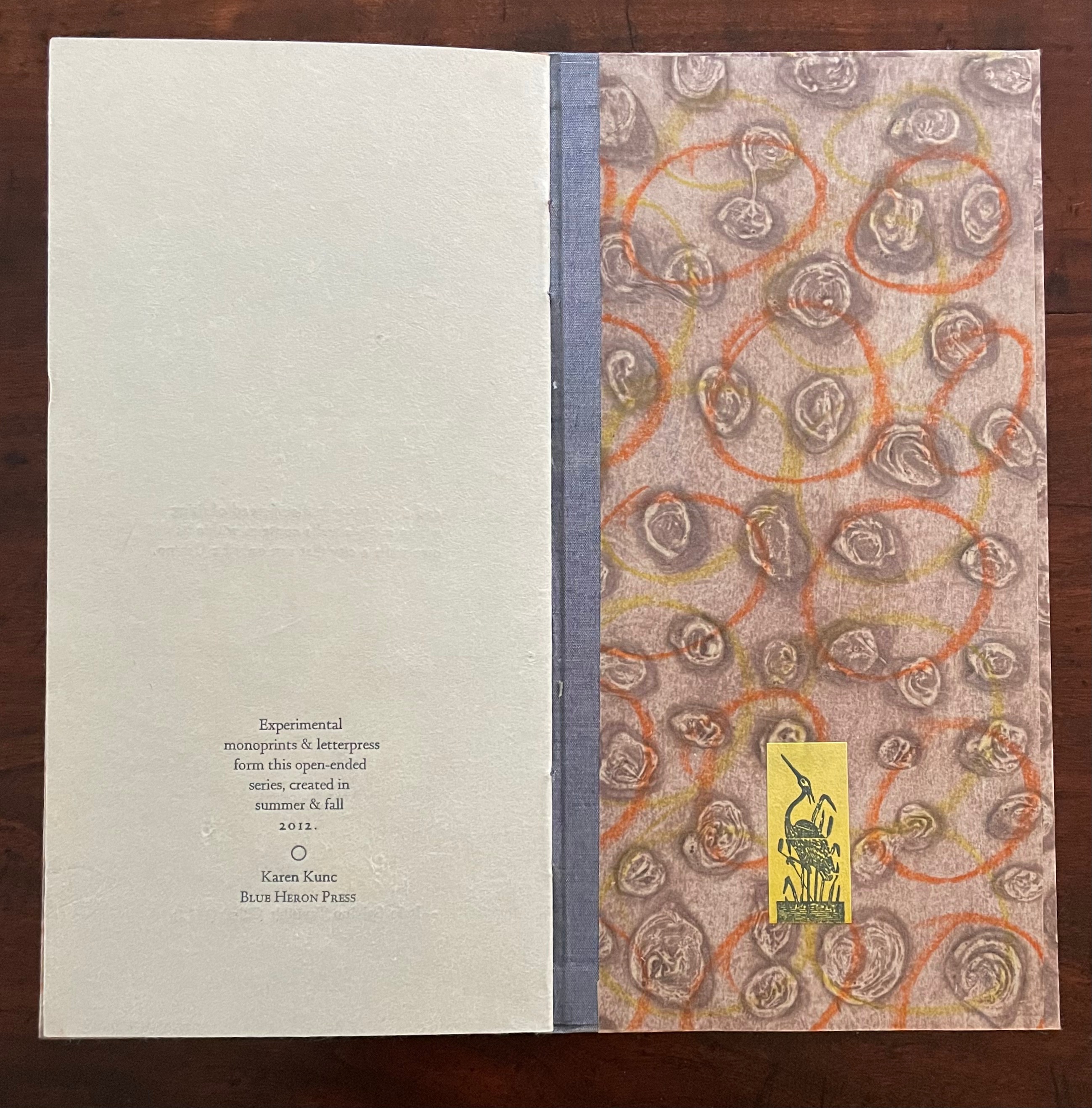 A closed booklet featuring artistic designs in earthy tones with circles and swirls in the background, and text describing an experimental monoprint and letterpress series by Karen Kunc, published by Blue Heron Press.