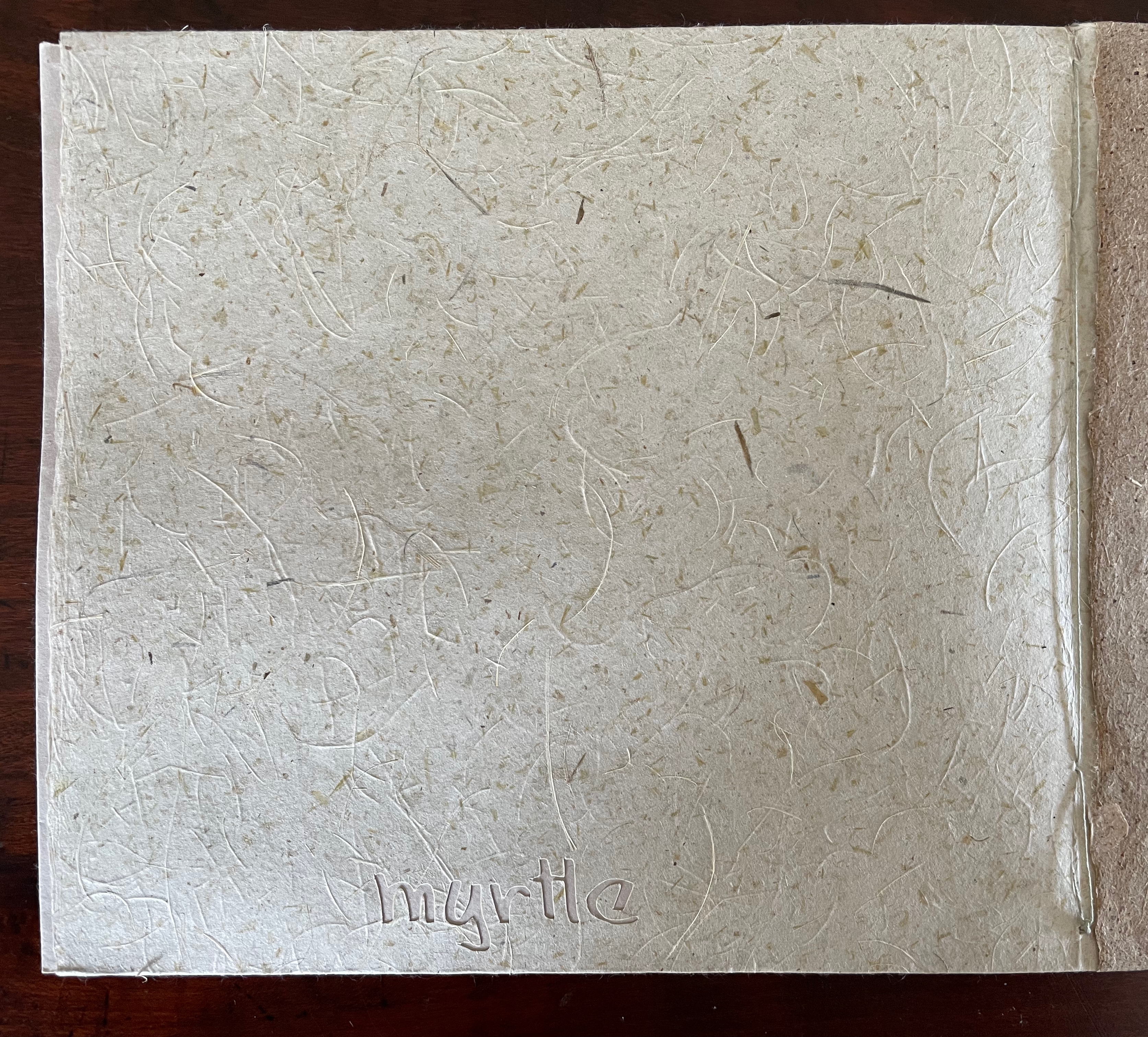 A close-up view of a textured, beige-colored page made from handmade paper, featuring natural fibers. The word 'myrtle' is embossed at the bottom left corner.