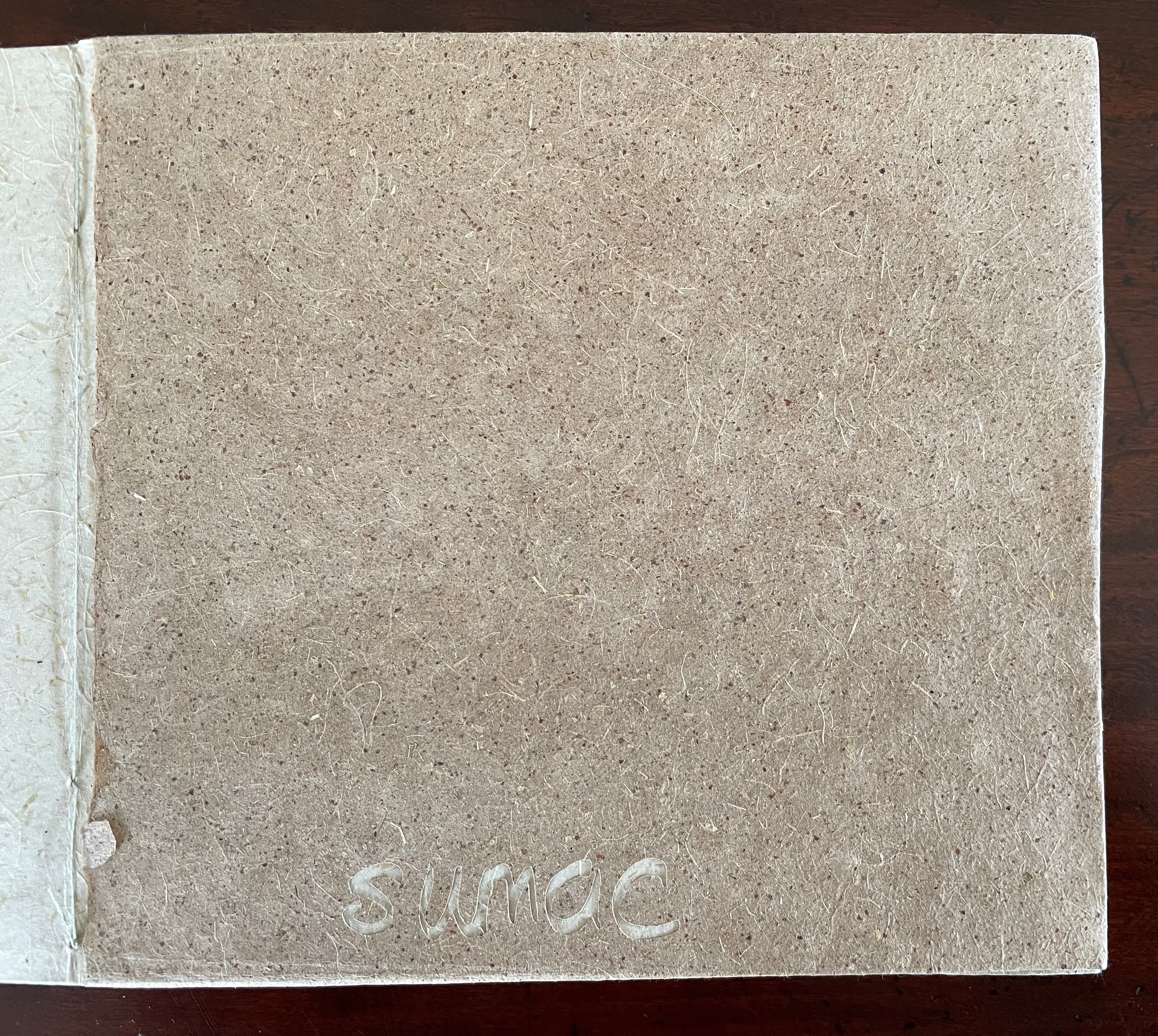 Close-up view of a textured, brown, unfinished book cover with a faintly visible handwritten title 'sundoc' at the bottom.