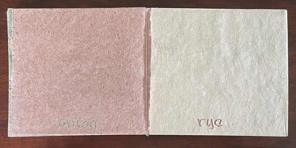 A spread of two pieces of handmade paper: one is a soft pink color with the word 'onion' written in green, and the other is a pale cream color with the word 'rye' written in light pink.
