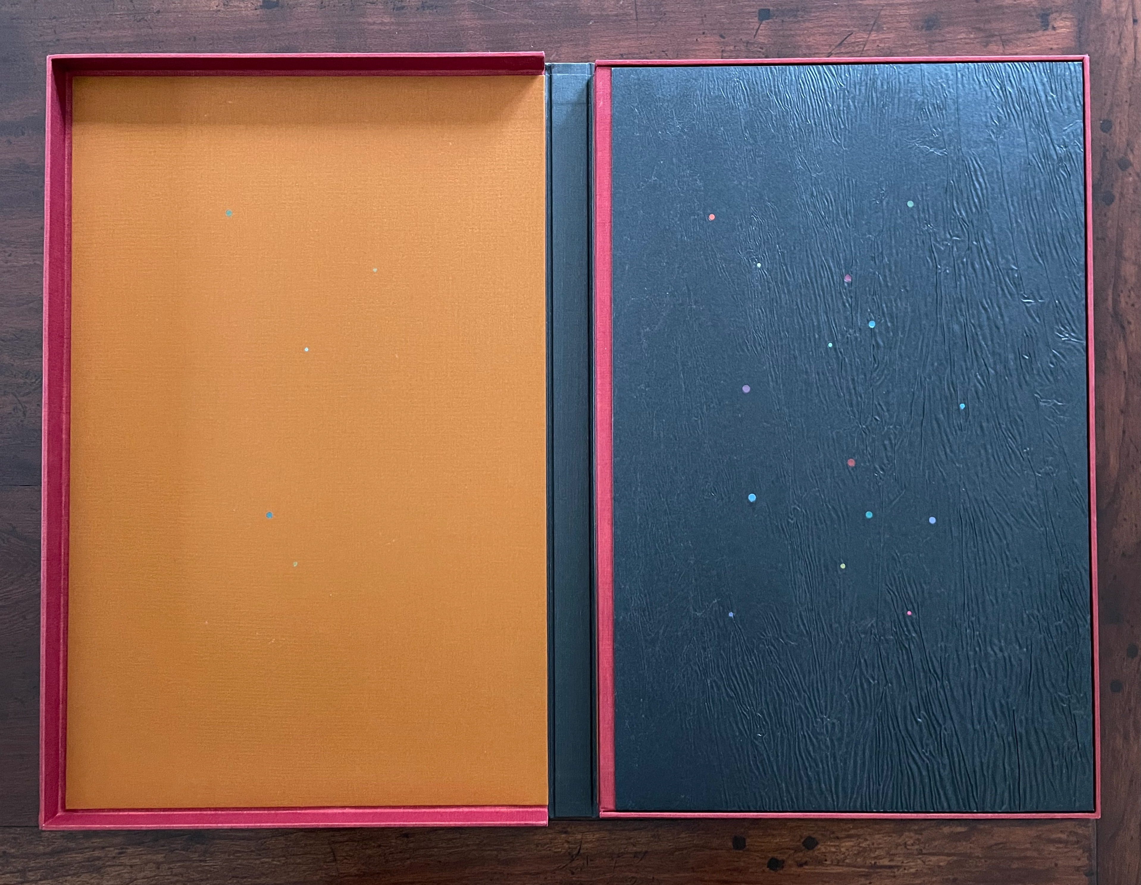 Opened box with an orange interior on the left and a textured black cover with colorful dots on the right.