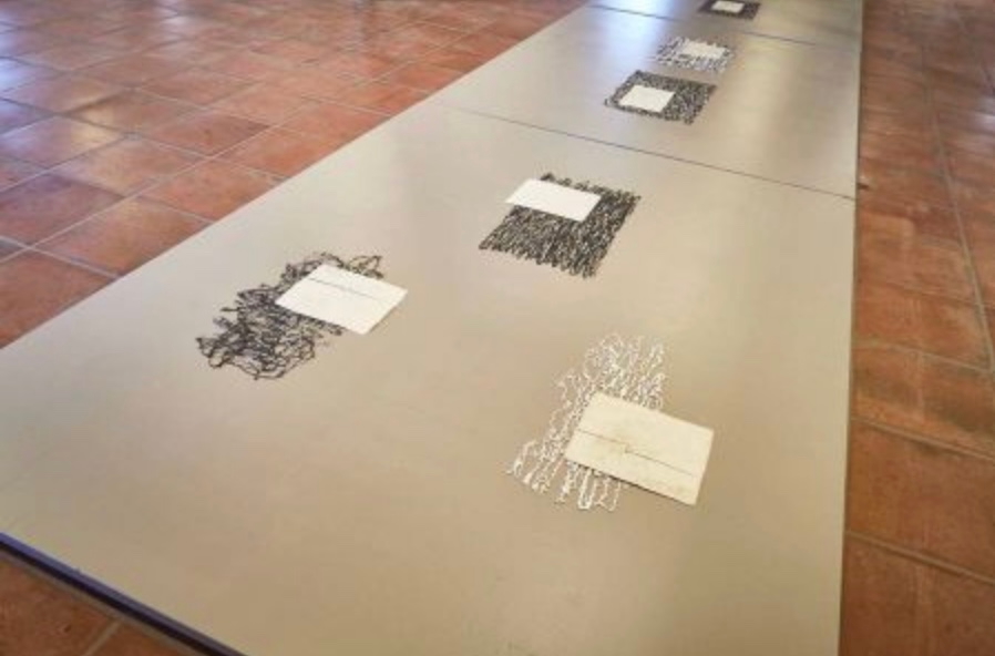 An installation consisting of several rectangular panels on the floor, each featuring abstract arrangements of black and white materials, accompanied by small blank labels.