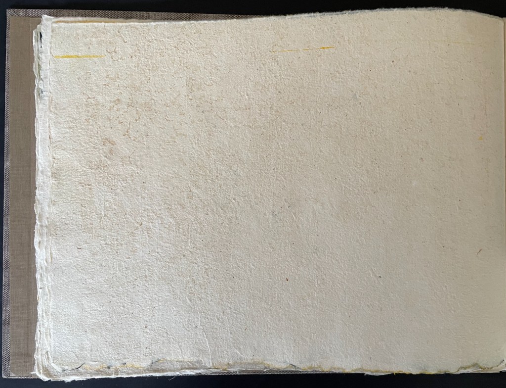 A blank, textured page from a book, showing a natural paper surface with minimal markings, bordered by a dark cover.