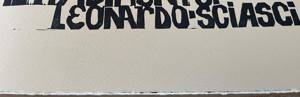 Close-up of black text on a textured cream background, featuring the name 'Leonardo Sciascì.'