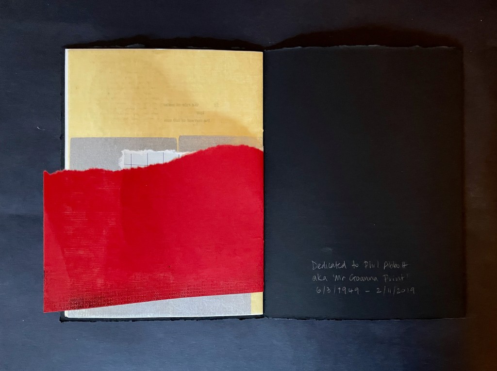 An open book with a yellow page on the left and a black page on the right, featuring a red fabric or paper strip crossing over the pages. The right page has handwritten text dedicating the book to Phil Abbott, including his birth and death dates.