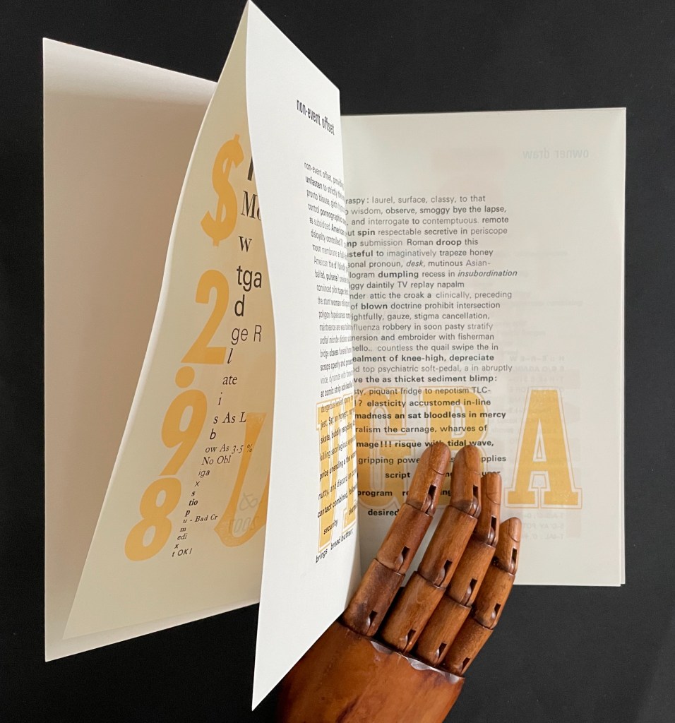 An open book with artistic text on the pages, featuring yellow typography and abstract designs, alongside a wooden mannequin hand resting on the table.