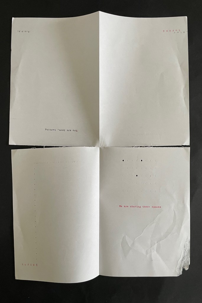 An open, blank book or magazine with minimalist design, featuring text on various pages like 'You are here', and 'We are sharing these spaces', alongside printed dots and shapes.