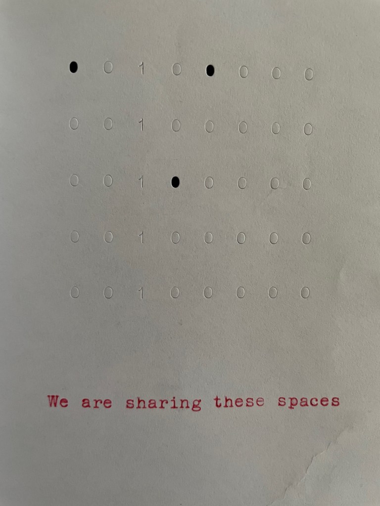 A textured paper with a pattern of embossed dots and binary numbers (0s and 1s), accompanied by the phrase 'We are sharing these spaces' printed in red text at the bottom.