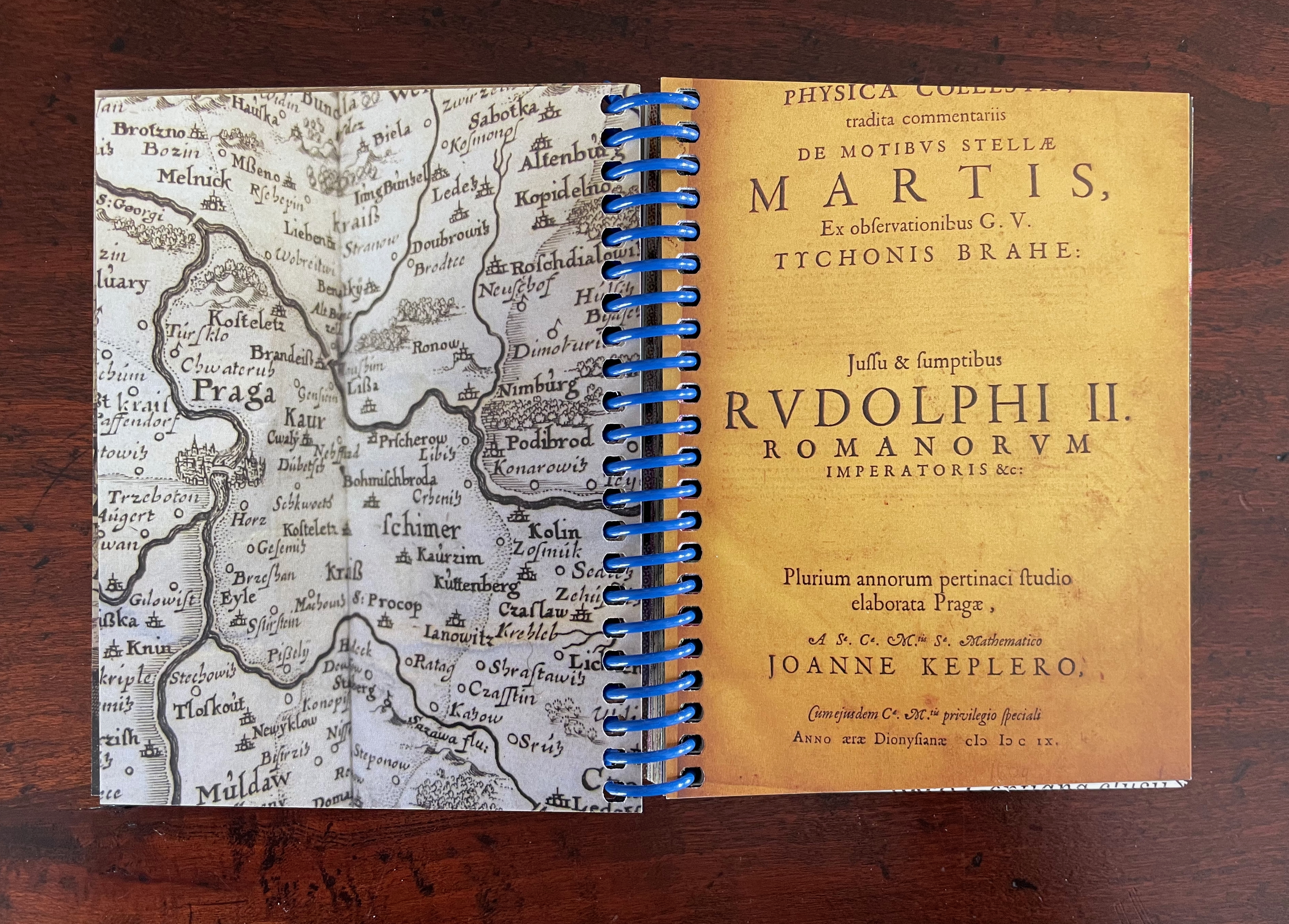 An open book with a map illustration on the left page and a title page on the right, featuring historical text and a blue spiral binding.