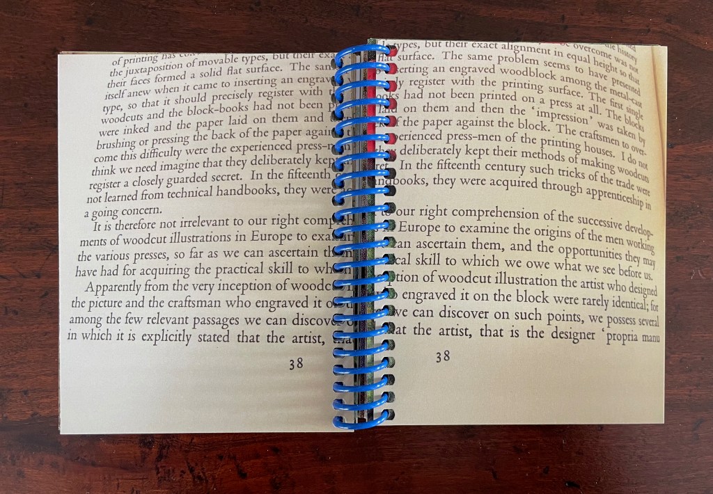 Open book with text on pages, showing blue and red spiral binding, viewed from above.