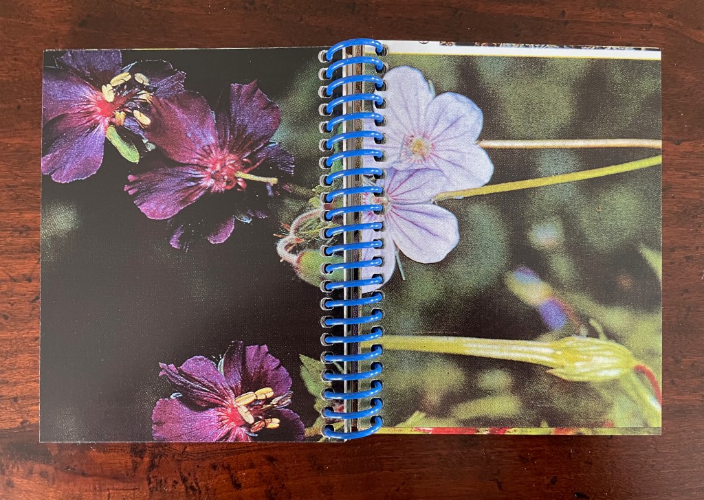 Open spiral-bound notebook with colorful images of flowers on pages, featuring purple and blue blossoms.