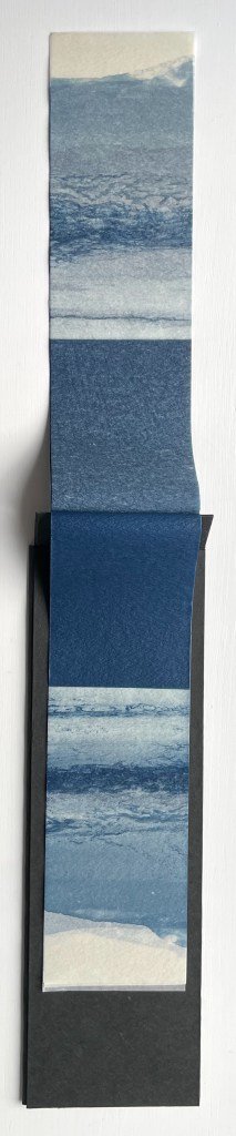 A vertical scroll of textured paper showcasing various shades of blue, resembling ocean waves, displayed against a dark background.