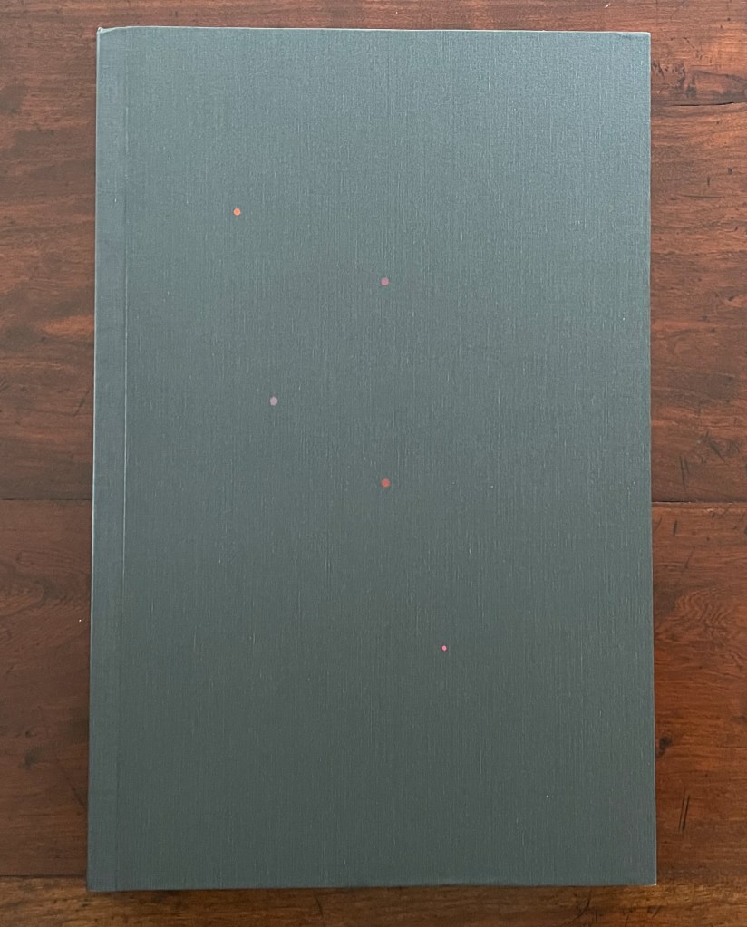 A closed book with a matte gray cover, featuring small colorful dots in red, pink, and orange scattered on the front.