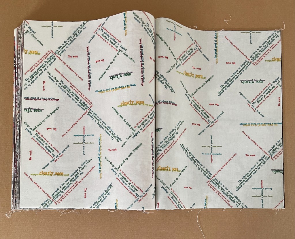 Open book displaying a patterned page with colorful text in various orientations, featuring phrases like 'clearly seen' and 'The work'.