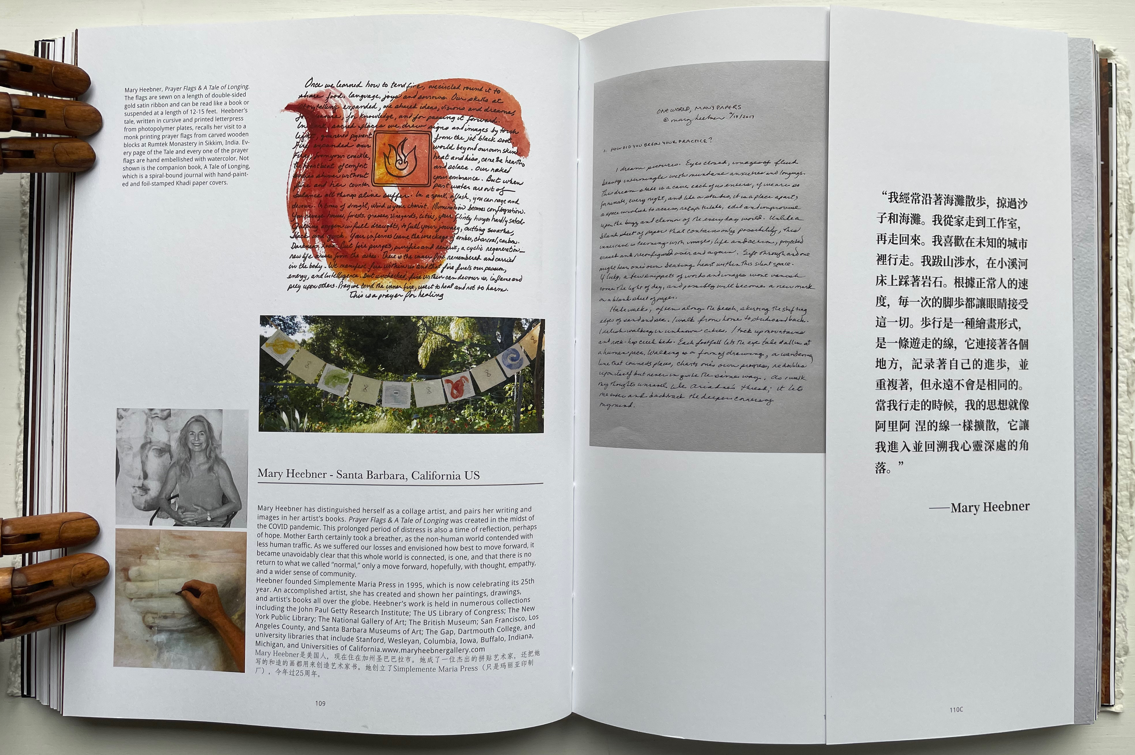 An open book page featuring artistic content, including text and illustrations. The left side presents a colorful illustration of a red and orange figure with text, while the right side includes handwritten notes and additional text in multiple languages. The page also features images of prayer flags and a collage by Mary Heebner, along with a brief bio.