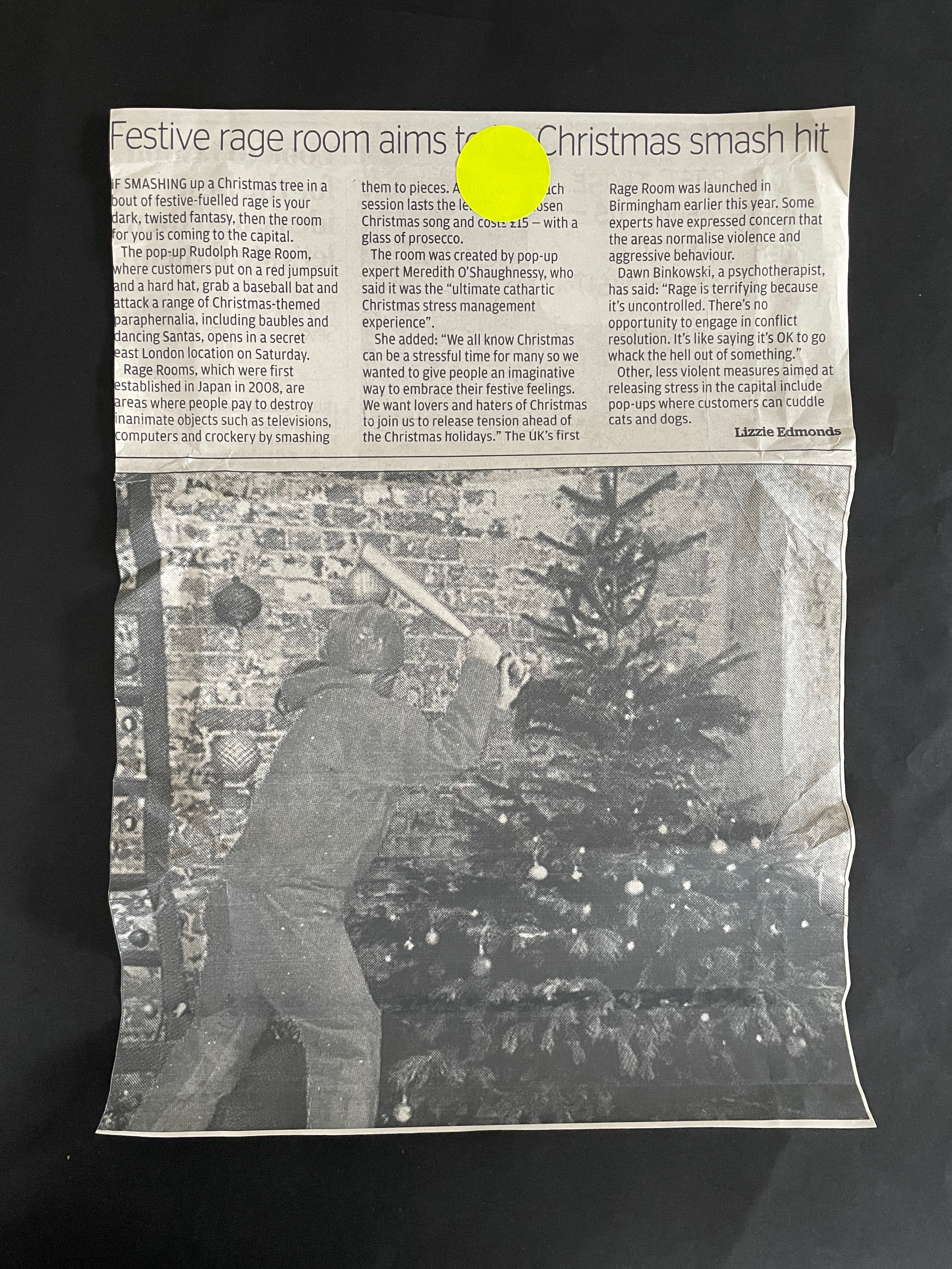 Black and white image of a person smashing a Christmas tree with a baseball bat in a festive setting, surrounded by decorations and presents. The photo is part of a newspaper article discussing a pop-up rage room experience.