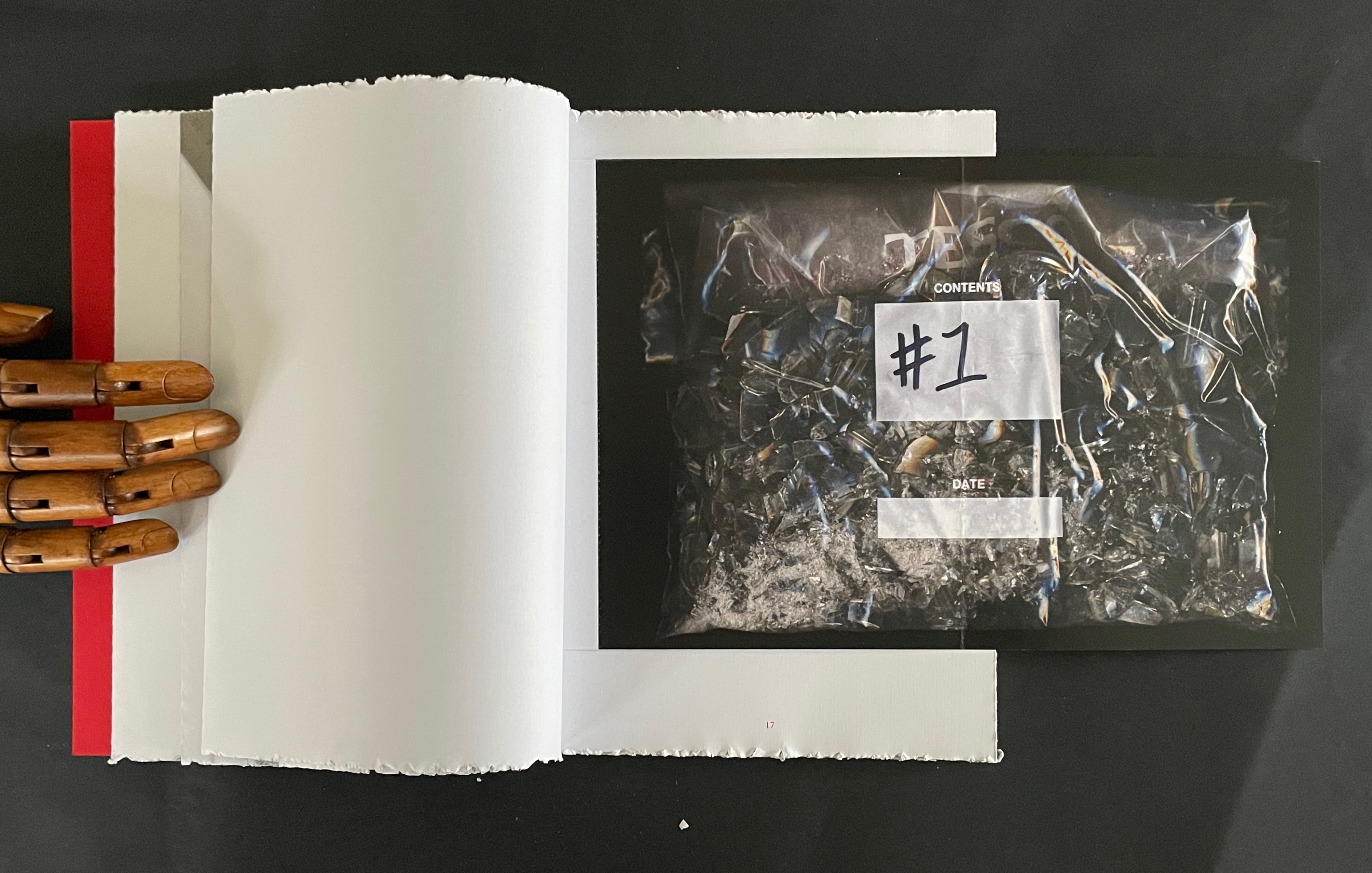 An open book displaying blank pages beside a plastic bag filled with small, colorful items labeled '#1' on a black background.