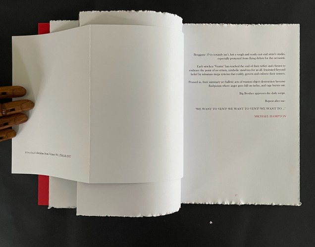 An open book with a textured white page on the right displaying text, and a partially visible red page on the left, with a hand holding the book.