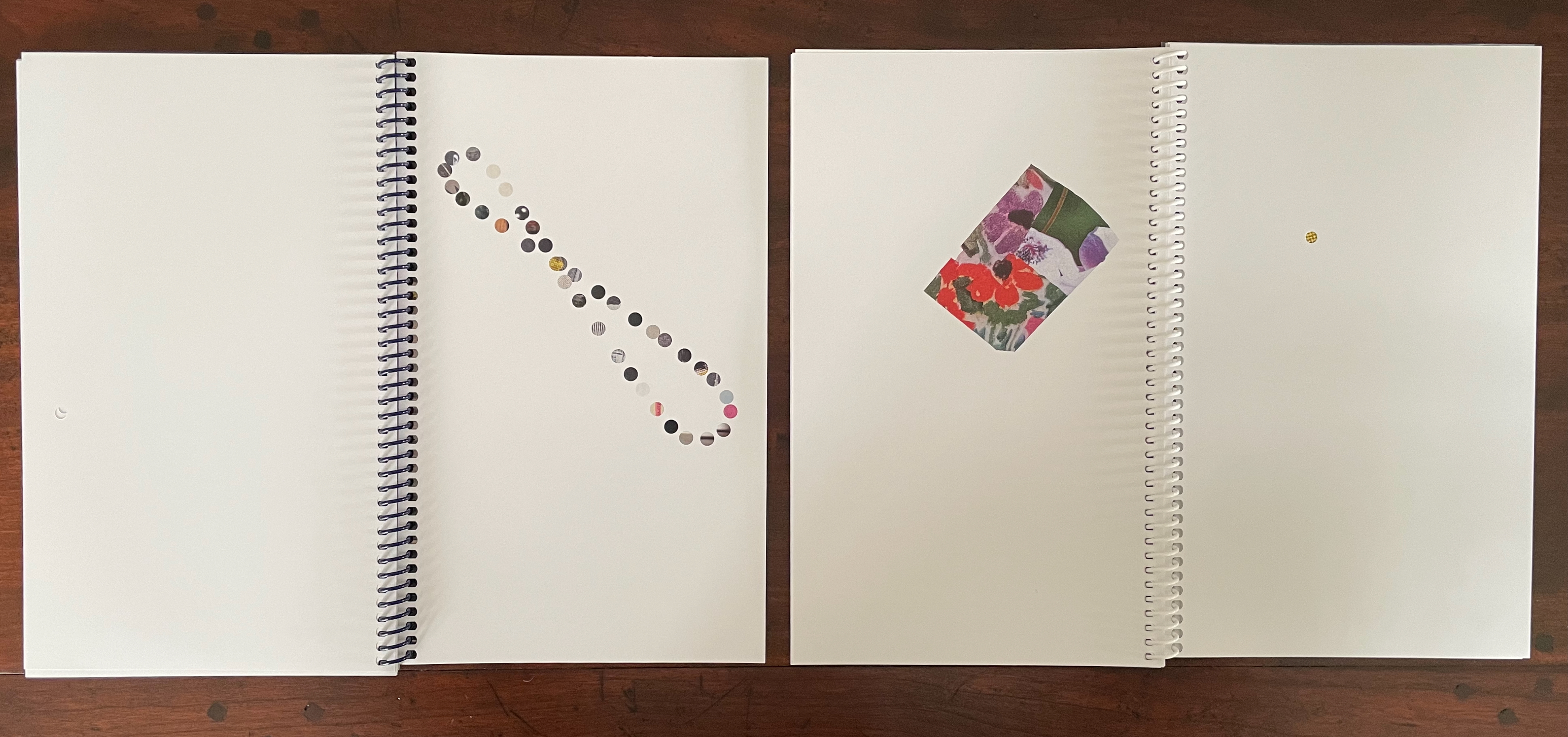 Two open spiral-bound sketchbooks on a wooden surface. The left book contains a line of colorful dots arranged in a wavy pattern, while the right book has a rectangular colorful floral sticker placed on its page.