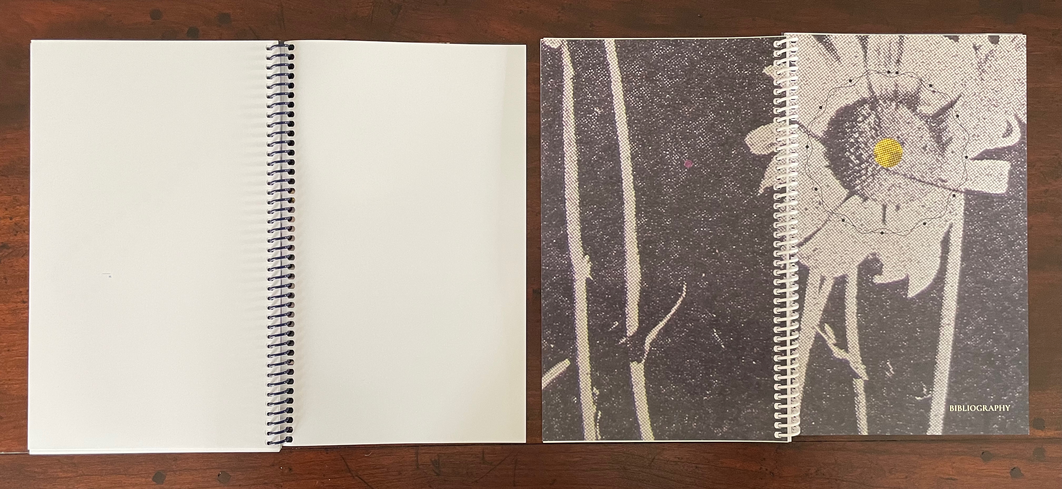 A blank spiral notebook on the left and a decorated spiral notebook featuring a floral design on the right, both displayed against a wooden surface.
