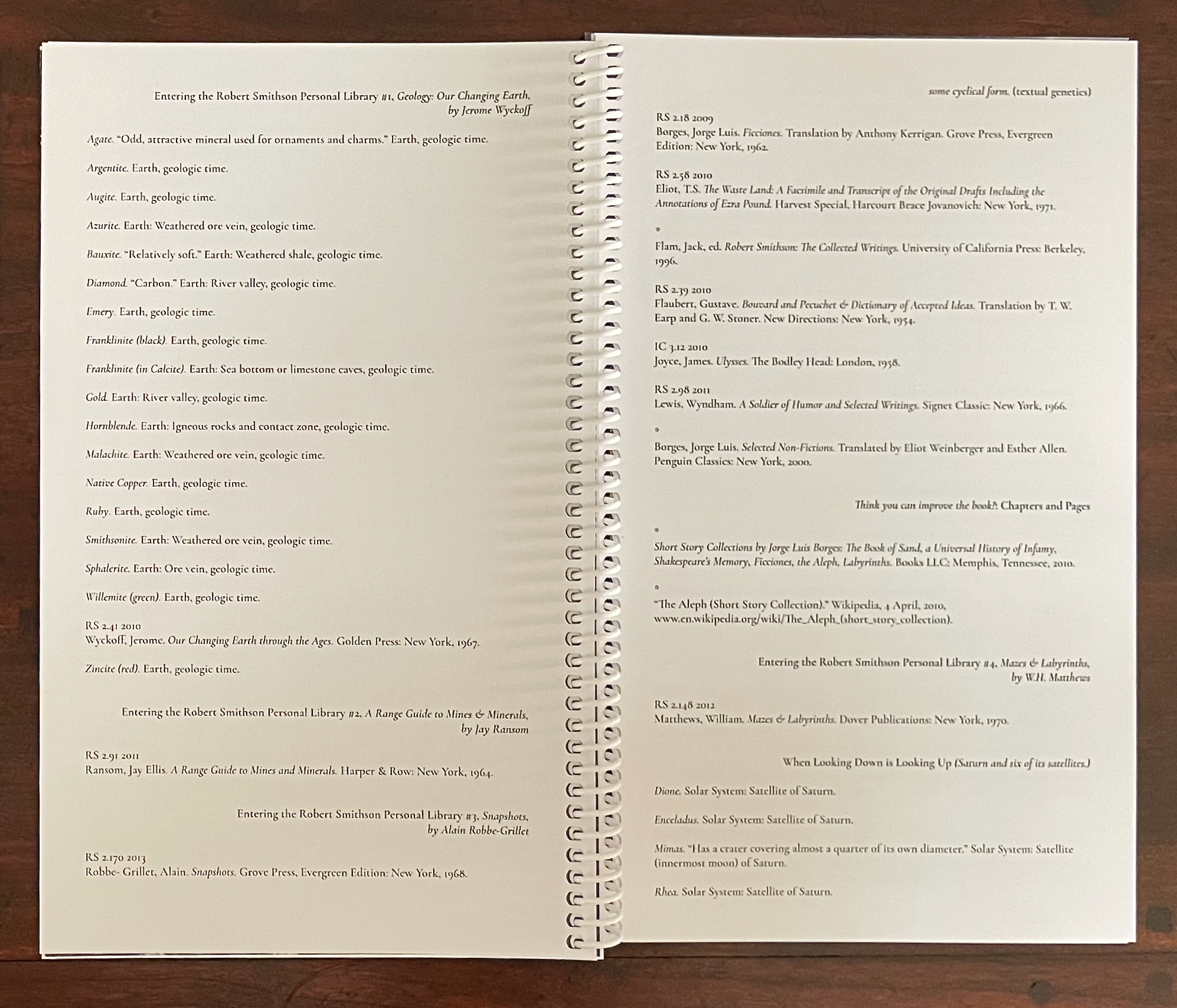 A close-up of an open spiral-bound book displaying a list of minerals, their descriptions, and references related to geology, along with bibliographic entries for various texts associated with the Robert Smithson Personal Library.