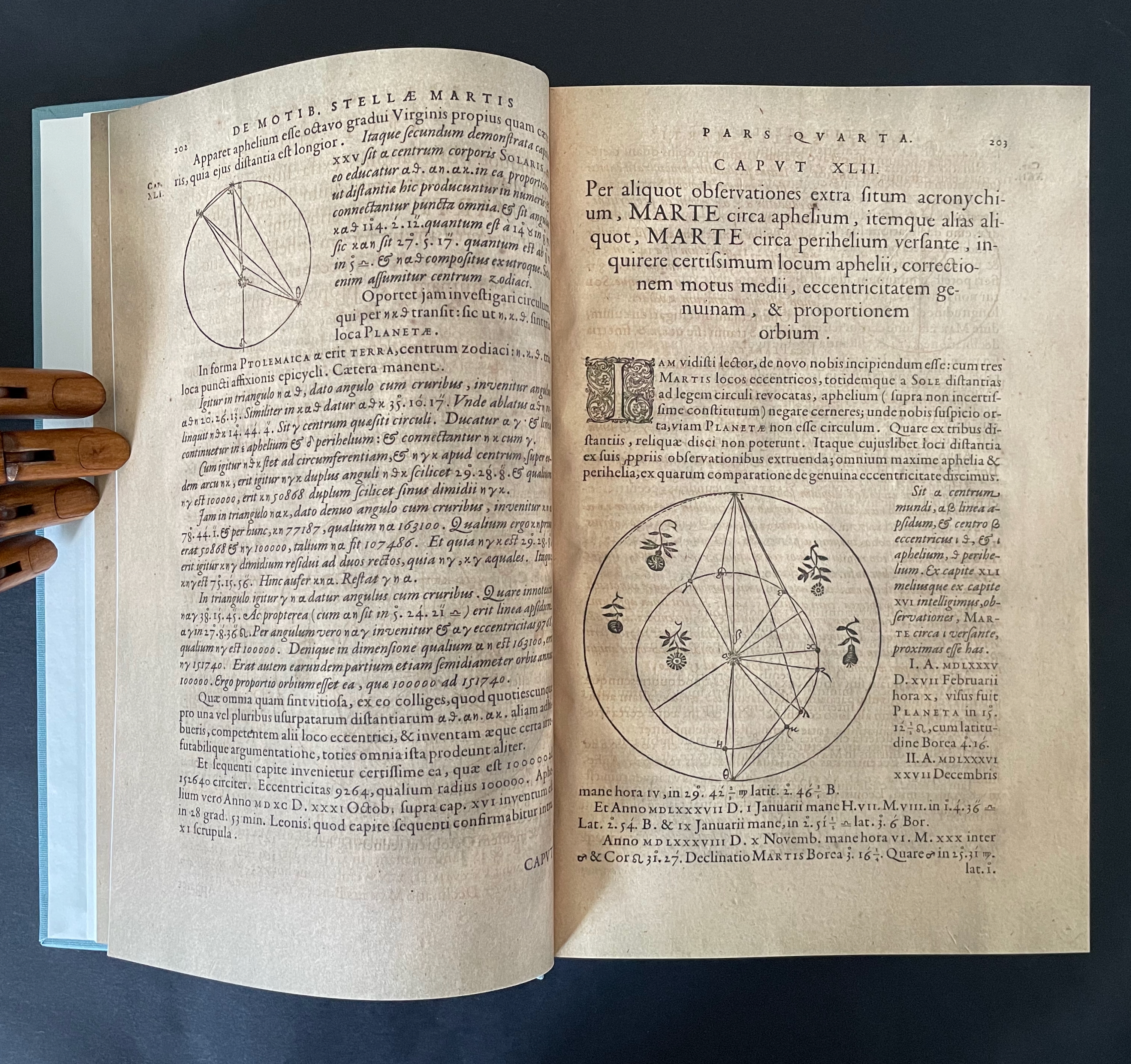 Open ancient book page with handwritten text in Latin, featuring diagrams related to astronomy, including a circular chart and illustrations of celestial movements.