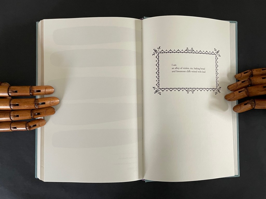 An open book with blank pages on the left and a decorative poem on the right, framed by a border, with wooden mannequin hands on both sides.