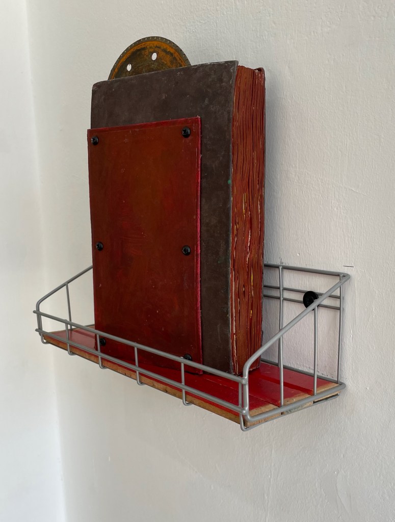 A metal wire shelf attached to a wall, holding a large, thick book with red and brown covers.