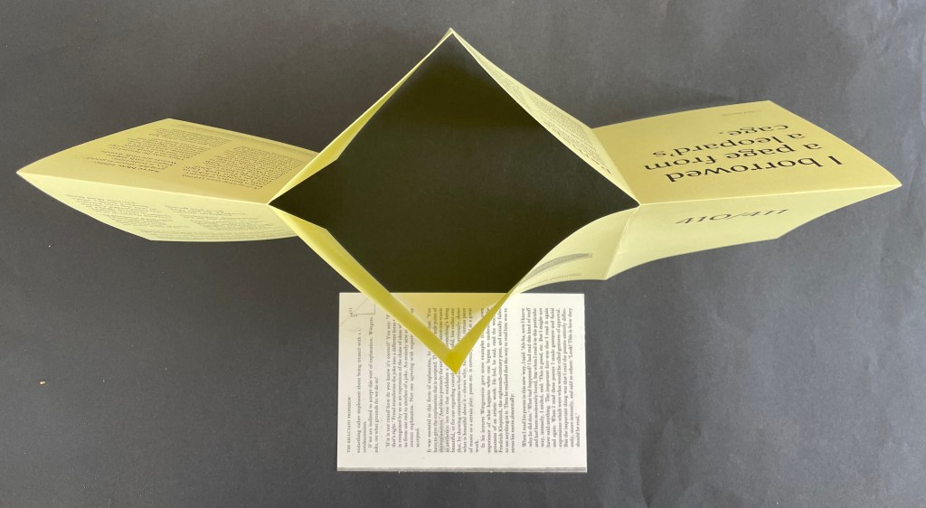Open yellow brochure with text, revealing a central folded section, placed over a sheet of paper with printed text beneath.