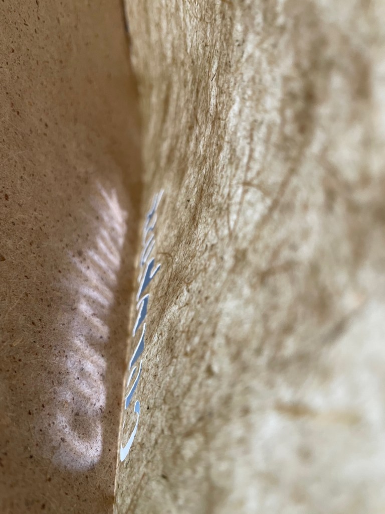 Close-up view of textured brown paper with soft light casting a shadow and faint reflections.